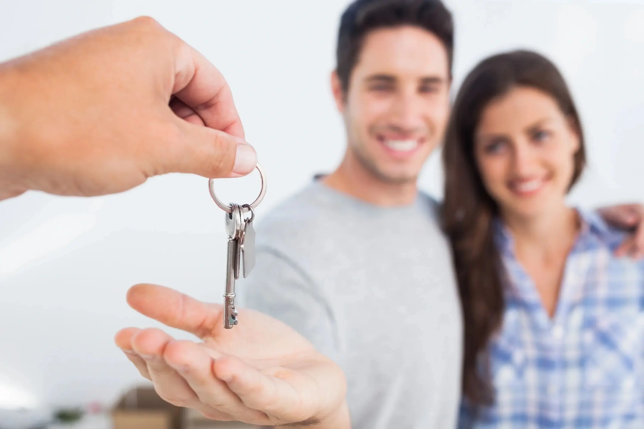 Couple receiving house keys, smiling in background.