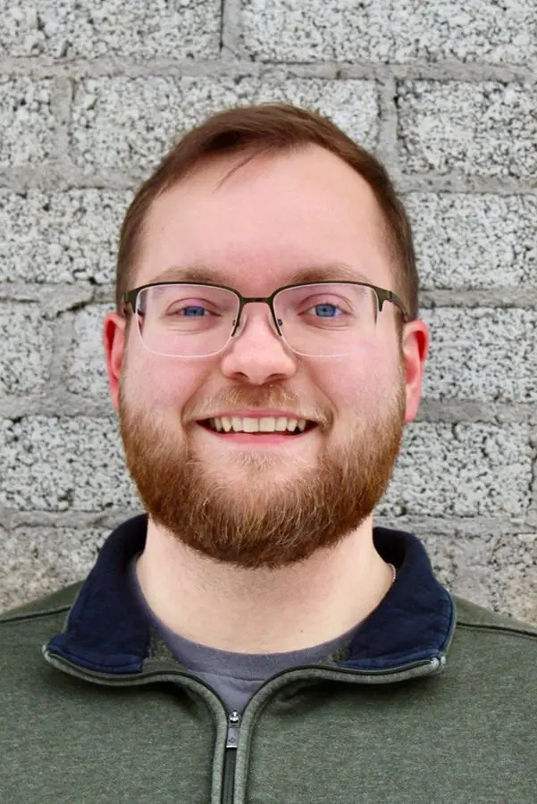 Smiling man with glasses against brick wall.