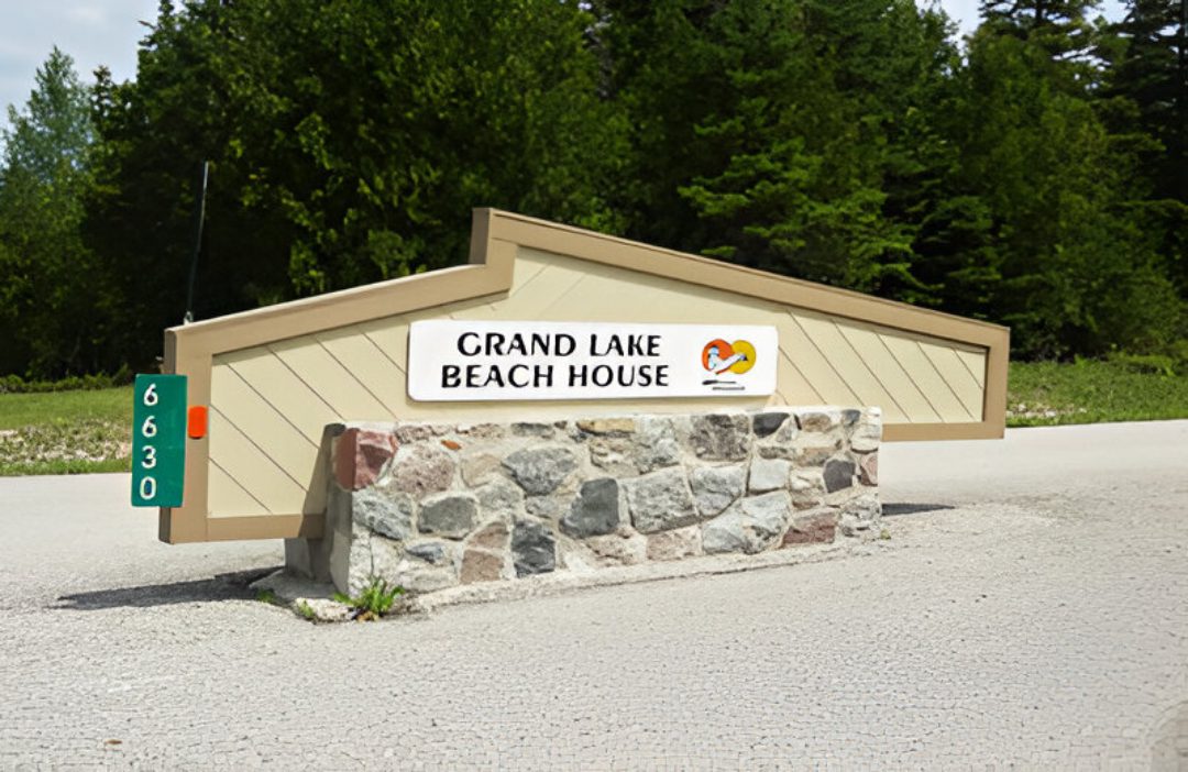 The Grand Lake Beach House sign on a stone base with trees in the background.
