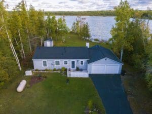 Lakeside house with trees and driveway.