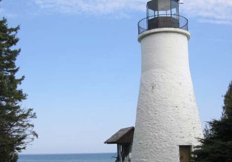 A white lighthouse stands near a calm sea under a clear blue sky.