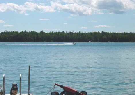 A serene lake with a motorcycle on the dock and a boat in the distance.