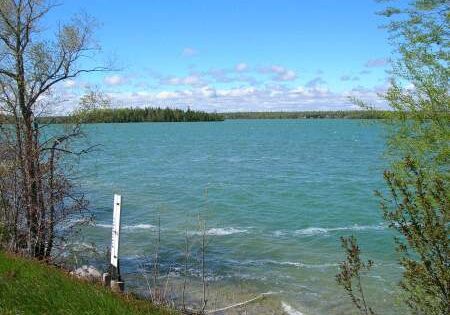 A calm lake under a blue sky with scattered clouds.