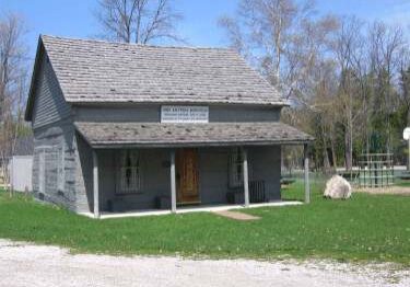 Old wooden cabin with a porch in a rural setting.