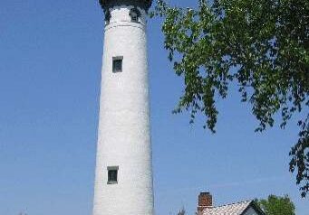 Tall white lighthouse next to a small house under a clear blue sky.